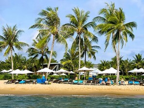 Una spiaggia con palme, sdraio e ombrelloni.