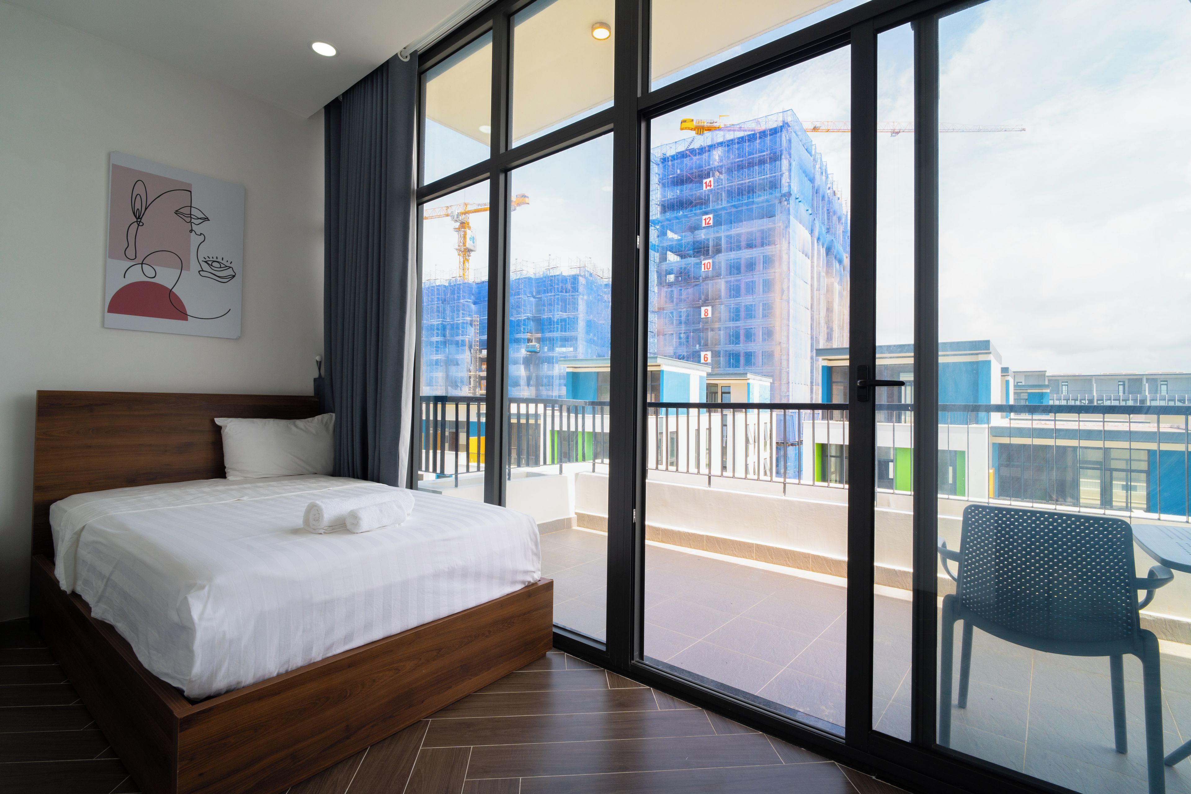 Habitación de hotel con una cama grande, vista a una obra en construcción y un balcón con una silla.