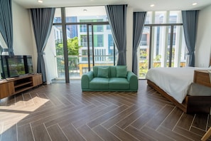 Une chambre d’hôtel moderne avec un canapé vert, un lit, une télévision et de grandes fenêtres avec des rideaux.