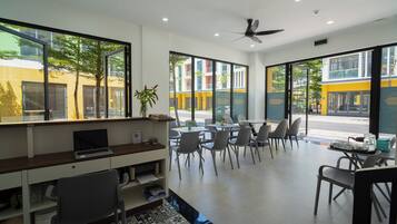 A modern cafe with a laptop on a desk, chairs around a table, and large windows offering a view of the street.