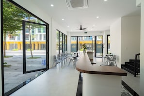 A modern interior with a long counter, seating area, and large windows offering a view of the street. - MeyBeach Apartment & Hotel Phu Quoc (Phu Quoc)