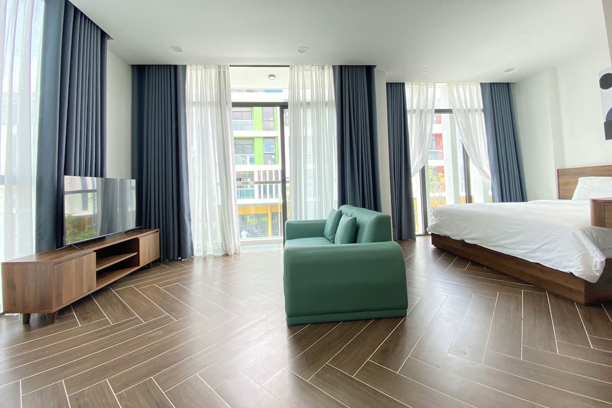 Ein modernes Hotelzimmer mit einem großen Bett, einem grünen Sofa, einem Fernseher auf einem Holztisch und einem Balkon mit Vorhängen.