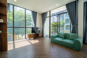 A modern living room with a green sofa, wooden entertainment unit, and large windows with curtains. - MeyBeach Apartment & Hotel Phu Quoc (Phu Quoc)