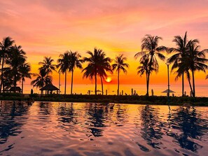 Een zonsondergang met palmbomen en een strand.