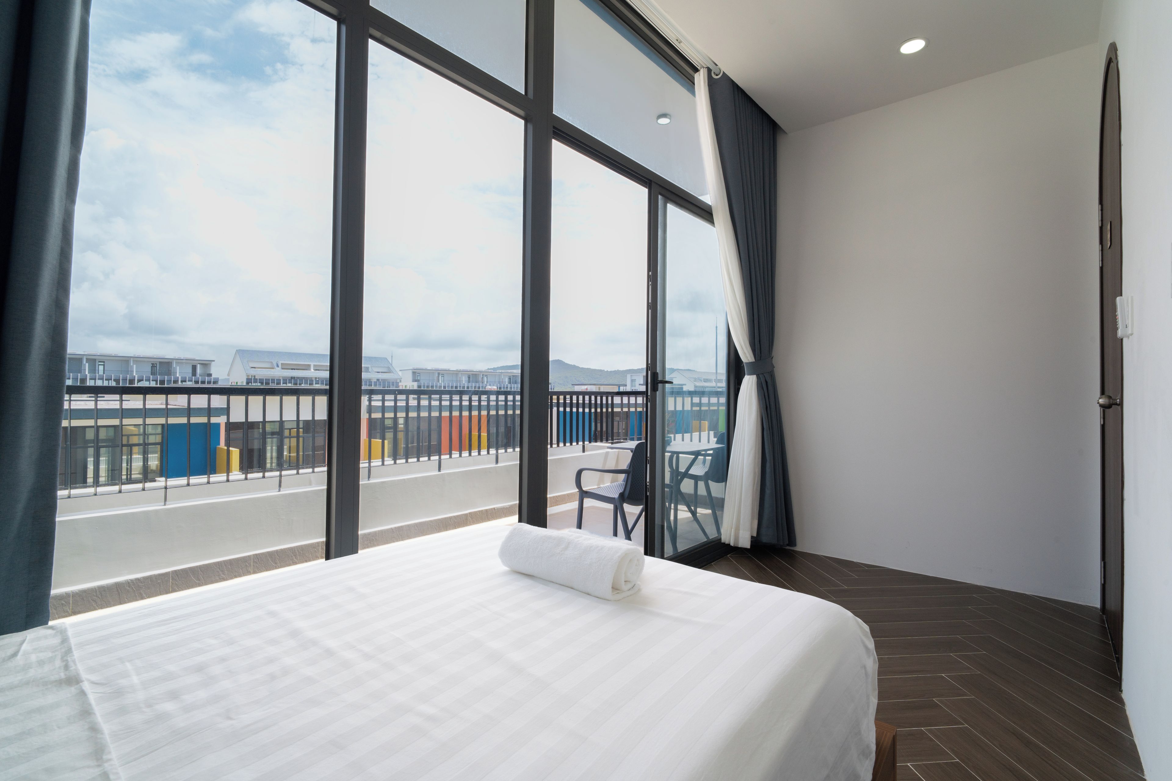 A hotel room with a large bed, a view of the cityscape, and a balcony with a table and chairs.