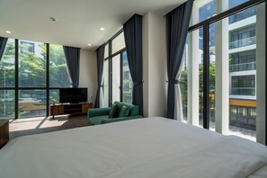 Una habitación de hotel moderna con una cama grande, un sofá verde, un televisor sobre un soporte de madera y amplias ventanas con vista a la ciudad.