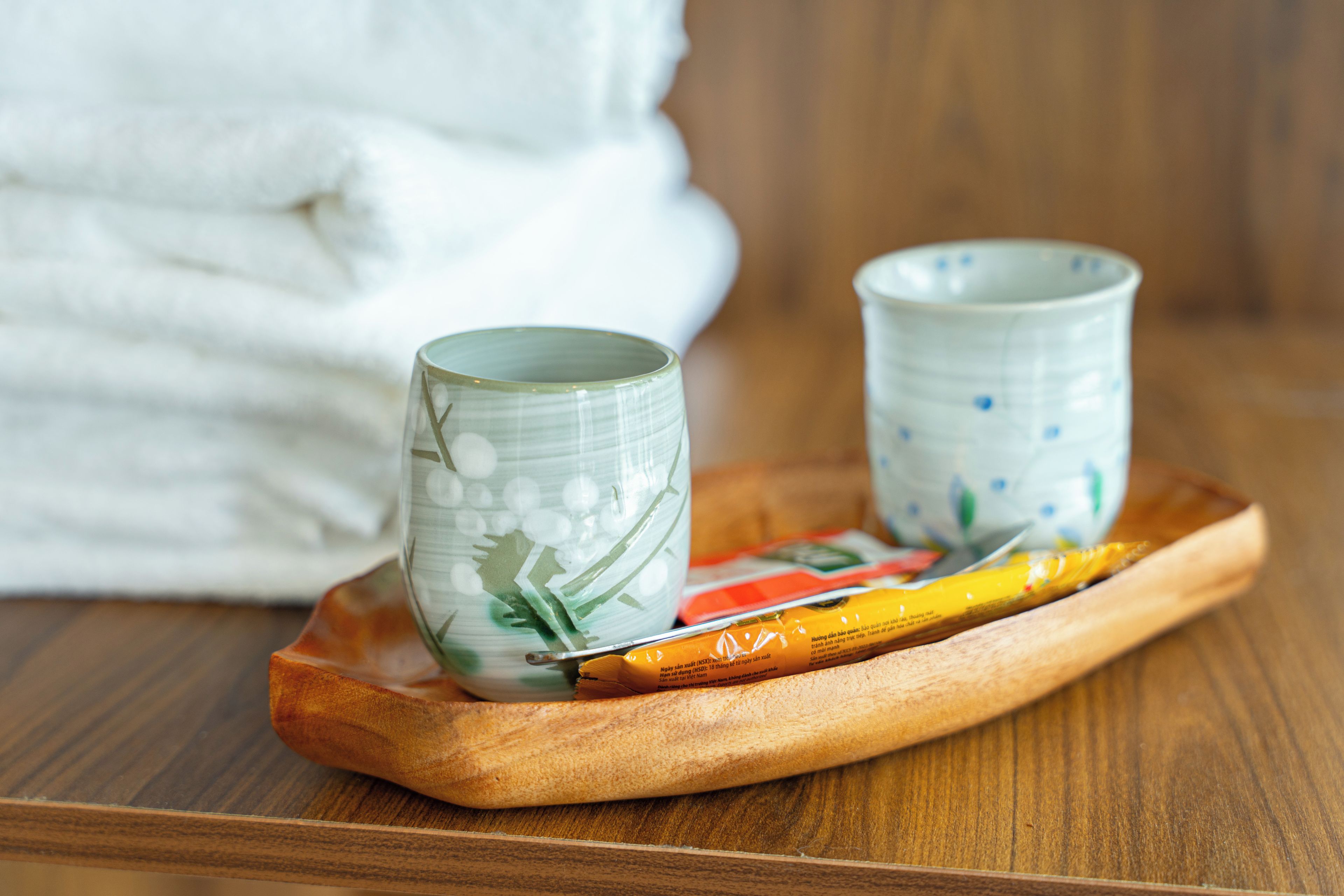 Two ceramic cups on a wooden tray with a towel in the background.
