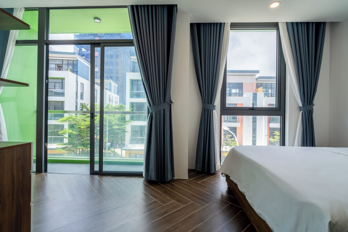 A hotel room with a bed, a large window, and a view of buildings outside.