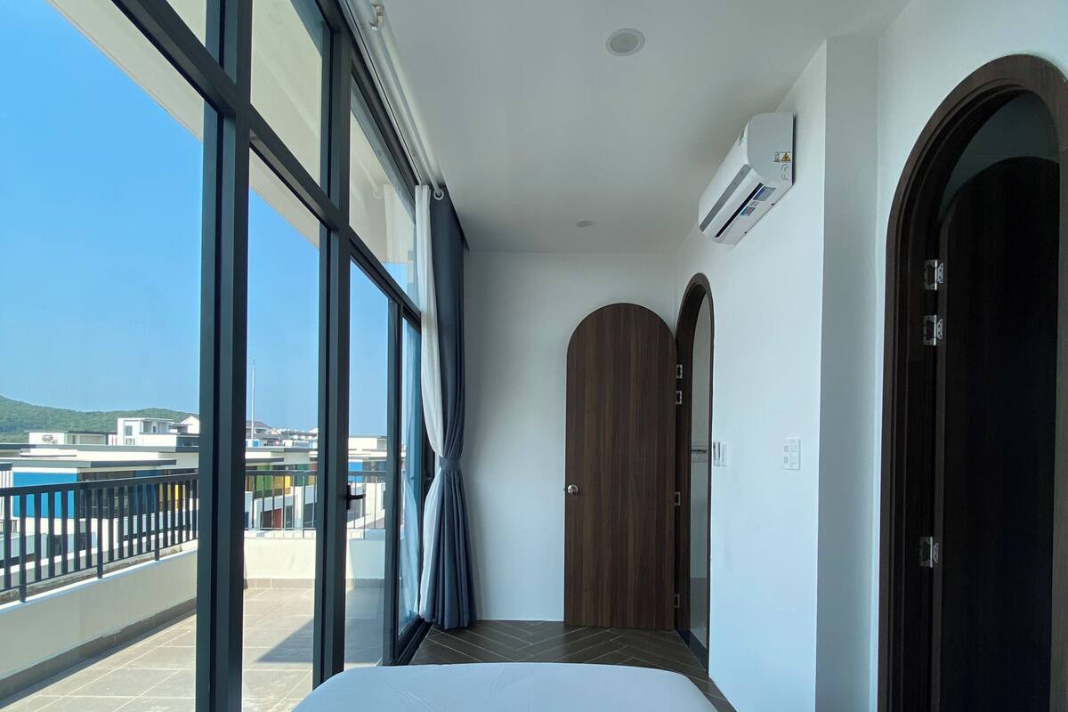 Ein Hotelzimmer mit einem großen Bett, Blick durch das Fenster und einer Tür zu einem weiteren Raum.