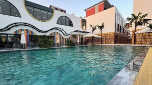 A swimming pool with clear water, surrounded by modern buildings with unique architecture, including curved lines and large windows.