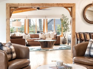Ein geräumiges Wohnzimmer mit Holzbalkendecke, einem großen Fenster, einem braunen Ledersofa und einem Couchtisch.