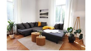 Ein modernes Wohnzimmer mit einem Ecksofa, zwei Holztischen, einer Topfpflanze und einer Stehlampe.