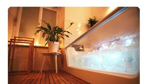 Ein Wellnessbereich mit Holzboden, einer Zimmerpflanze, einem Sessel und einer Badewanne mit Wasser.