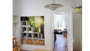 Ein Zimmer mit einem Holztisch, einem Bücherregal und Blick in einen weiteren Raum mit einer Couch und einem Fenster.