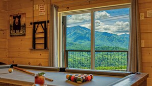 Una mesa de billar con vistas a un paisaje montañoso a través de una ventana.