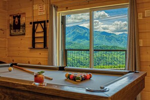 Ein Billardtisch mit Blick auf eine gebirgige Landschaft durch ein Fenster.