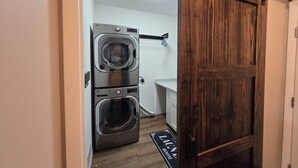Een wasserette met gestapelde wasmachines en drogers, een wit aanrechtblad en een houten deur.