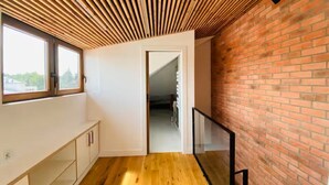 A room with a sloped wooden ceiling, a brick wall, a wooden floor, a glass railing, and a door leading to another room.