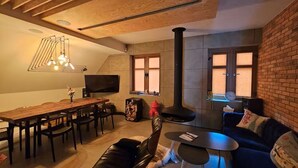 A modern living room with a wooden ceiling, a fireplace, a dining area with a long table and chairs, and a cozy seating area with a sofa and a small round table.