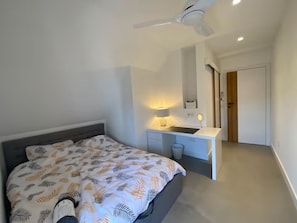 A bedroom with a bed, a bedside table with a lamp, a ceiling fan, and a door leading to another room. - Modern 3BD Apartment in Zolynia Town Square (Żołynia)