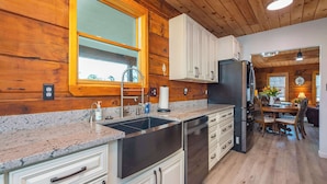 A kitchen with wooden walls, a granite countertop, stainless steel appliances, and a dining area with a table and chairs.