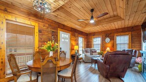 A wooden interior with a dining table, chairs, a sofa, and a ceiling fan.
