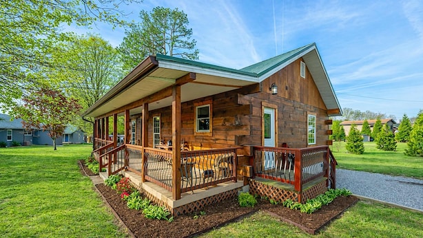 A wooden cabin with a porch, a covered deck, and a well-maintained lawn.