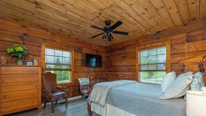 A wooden cabin bedroom with a bed, dresser, chair, and a ceiling fan.