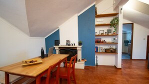 A dining area with a wooden table and chairs, a fireplace, and a bookshelf with various items. - Parede Coastal Family Retreat (Cascais)