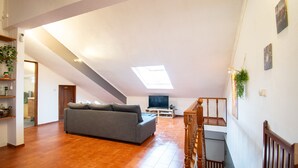 A spacious living area with a sofa, a TV, and a staircase. - Parede Coastal Family Retreat (Cascais)