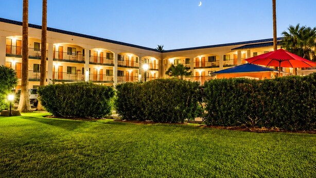 A multi-story hotel with a courtyard, palm trees, and a crescent moon in the sky. - Truestay Inn (Bakersfield)
