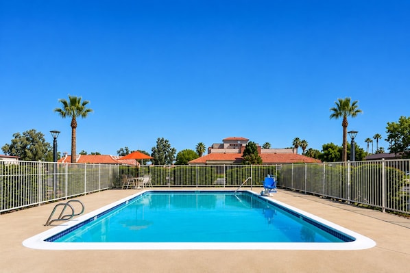 A rectangular swimming pool with a white edge, surrounded by a metal fence, and a clear blue sky above.