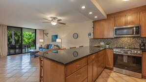 A modern kitchen with wooden cabinets, a microwave, and an oven. - Kamaole Sands Condo | Ground Floor, 2 Bath, Pool, Hot Tub, AC, Walk to Beach (Kihei)