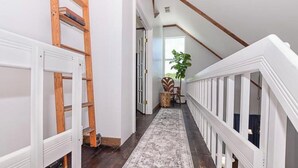 A narrow hallway with a wooden ladder, a white railing, and a rug leading to a door. - Coastal Retreat, Modern Home Near Beach! (Fort Pierce)