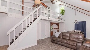 A spacious living area with a brown leather sofa, a white staircase, and a ceiling fan. - Coastal Retreat, Modern Home Near Beach! (Fort Pierce)
