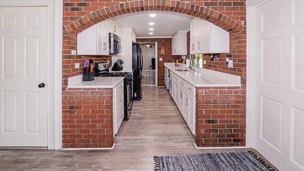 A hallway with a brick archway leading to a kitchen area with white cabinets and a microwave. - Coastal Retreat, Modern Home Near Beach! (Fort Pierce)