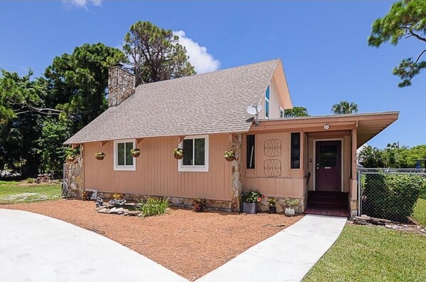 A single-story house with a sloped roof, a front porch, and a small front yard with plants.