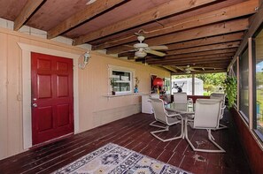 A covered patio with a red door, a ceiling fan, and a table with chairs.