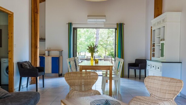 Een ruime woonkamer met een eettafel, rieten stoelen, een bank en een keuken met kastjes en een koelkast.