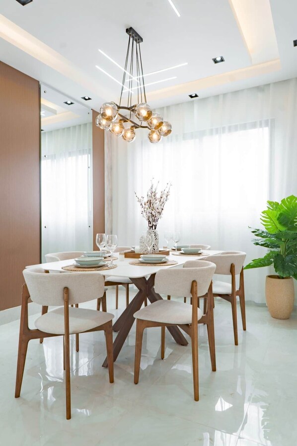 Una sala da pranzo moderna con un tavolo rotondo, sei sedie, un lampadario e una pianta in vaso.