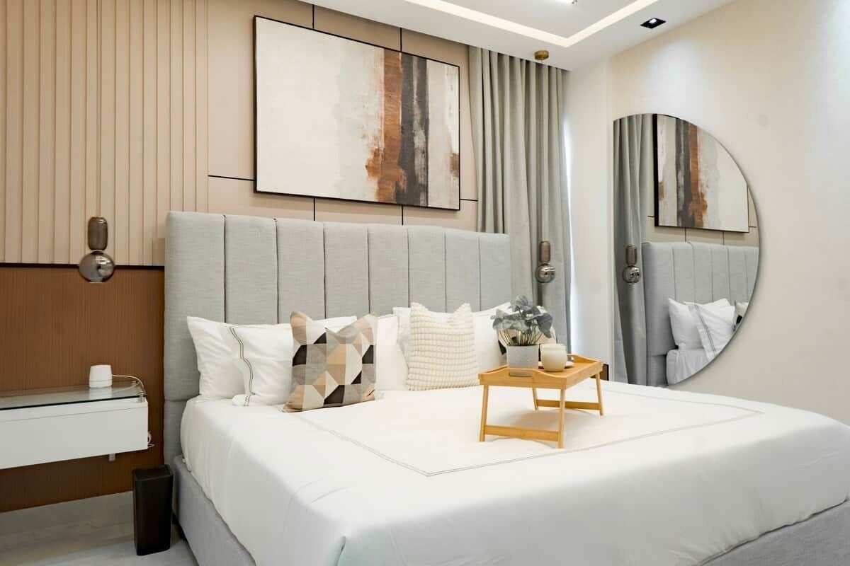 Une chambre à coucher moderne avec un grand lit, une table de chevet, un miroir fixé au mur et des œuvres d’art abstraites.
