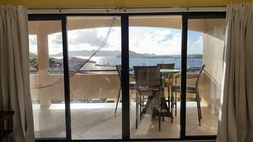 A room with a large sliding glass door leading to an outdoor terrace with a view of the sea and mountains.