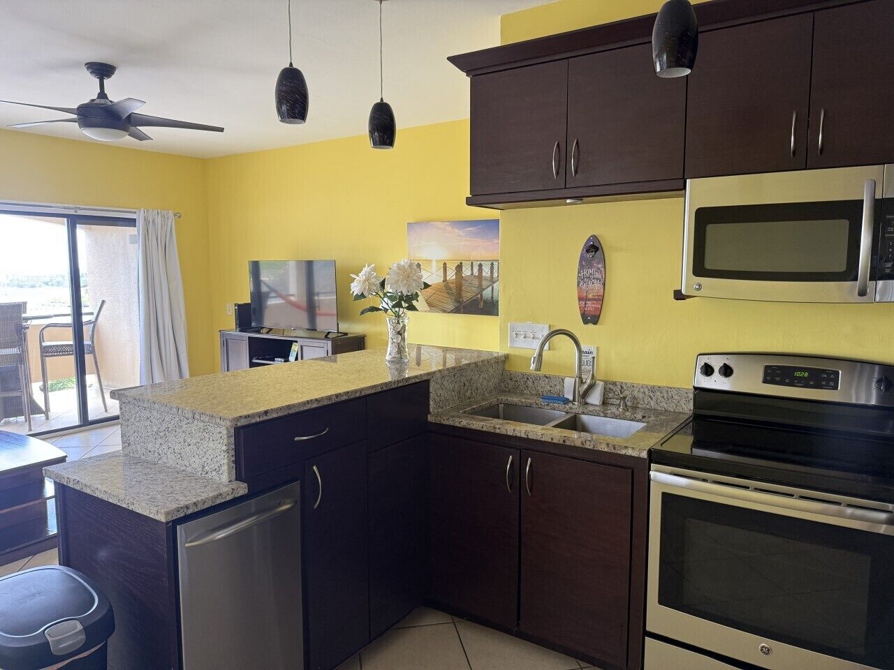 A kitchen with dark cabinets, a granite countertop, a microwave, an oven, and a ceiling fan.