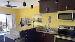 A kitchen with dark cabinets, a granite countertop, a microwave, an oven, and a ceiling fan. - Red Hook Retreat with Stunning Ocean Views (Red Hook)