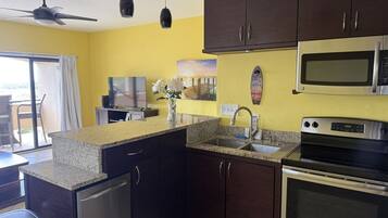 A kitchen with dark cabinets, a granite countertop, a microwave, an oven, and a ceiling fan.