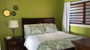 A bedroom with a bed, a nightstand with a lamp, a ceiling fan, and a window with blinds.