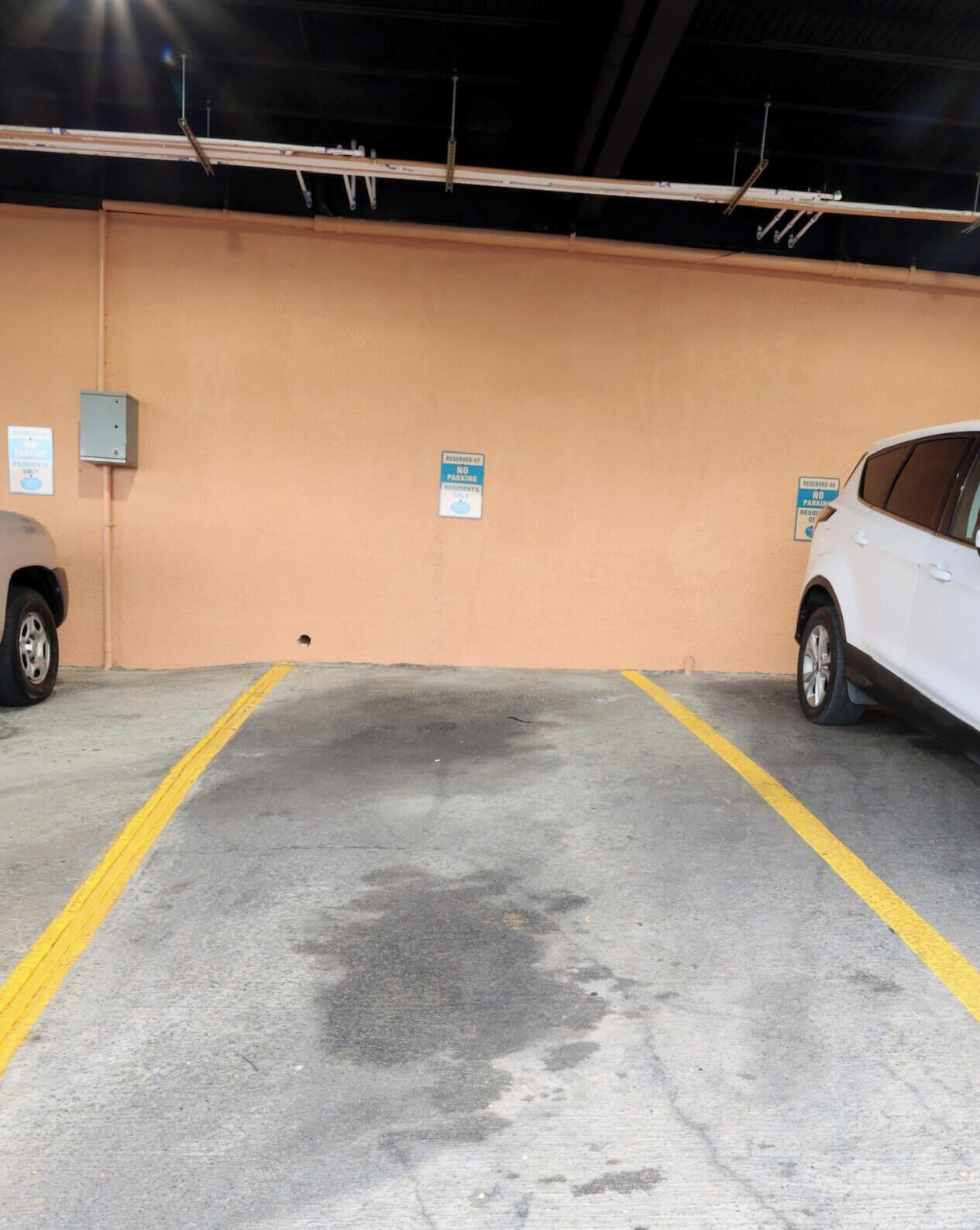 A parking garage with two cars parked, yellow lines on the floor, and signs indicating no parking.