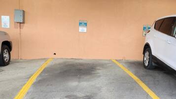 A parking garage with two cars parked, yellow lines on the floor, and signs indicating no parking.