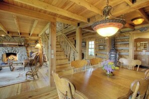Ein rustikales Holzinterieur mit Kamin, einem Esstisch mit Stühlen und einer Treppe.