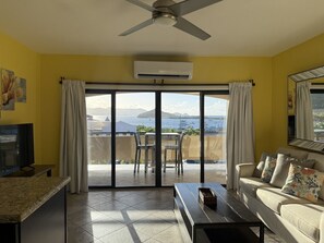 Ein Wohnzimmer mit einer Couch, einem Couchtisch, einem Fernseher und einem Balkon mit Tisch und Stühlen.
